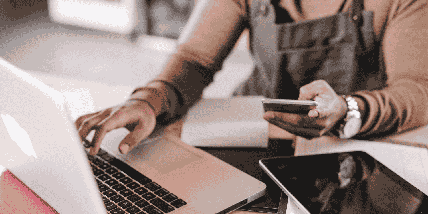 Business owner using a laptop and smartphone at a workspace, managing online giveaway campaigns to boost customer engagement and brand visibility.