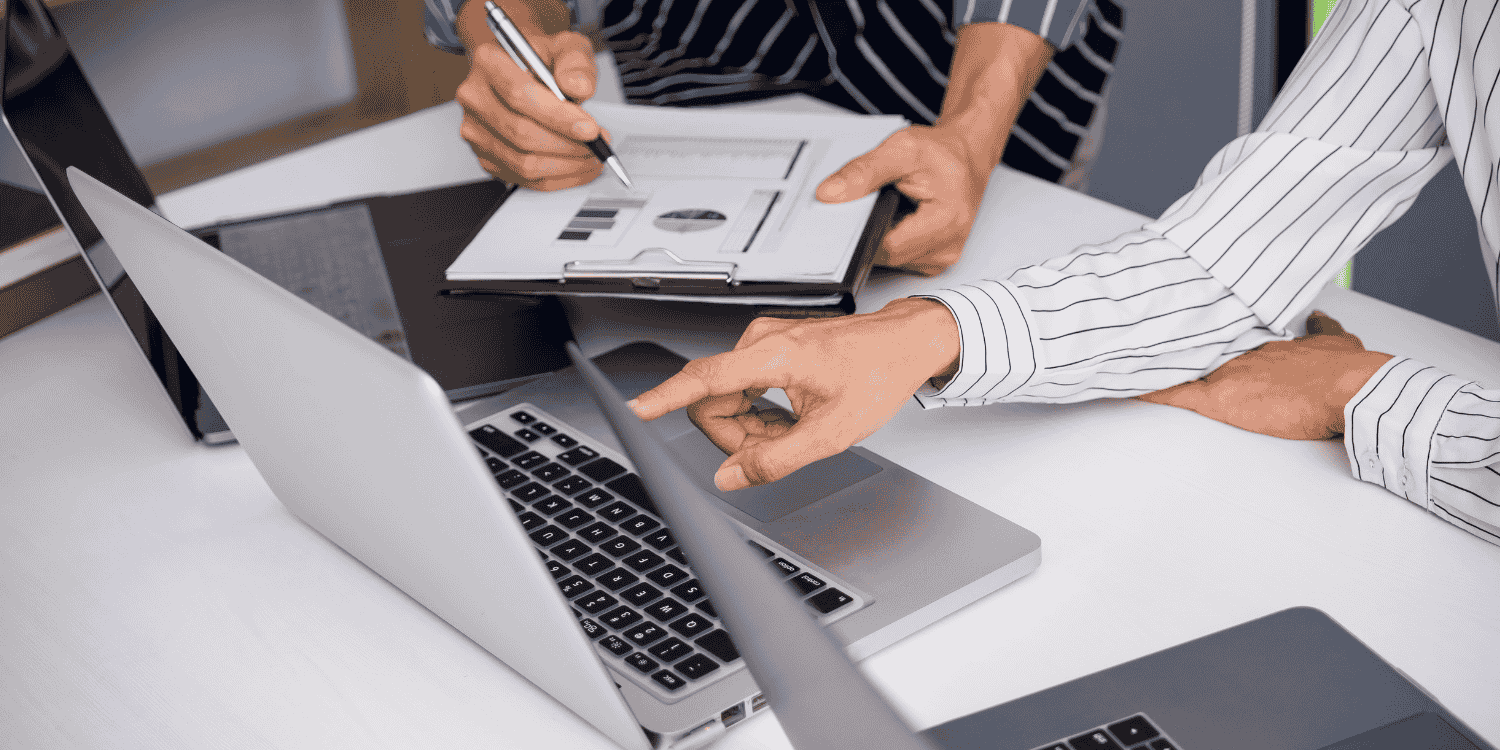 Two people reviewing charts and data on a clipboard and laptop, discussing strategy and performance metrics for organizing an effective giveaway campaign.