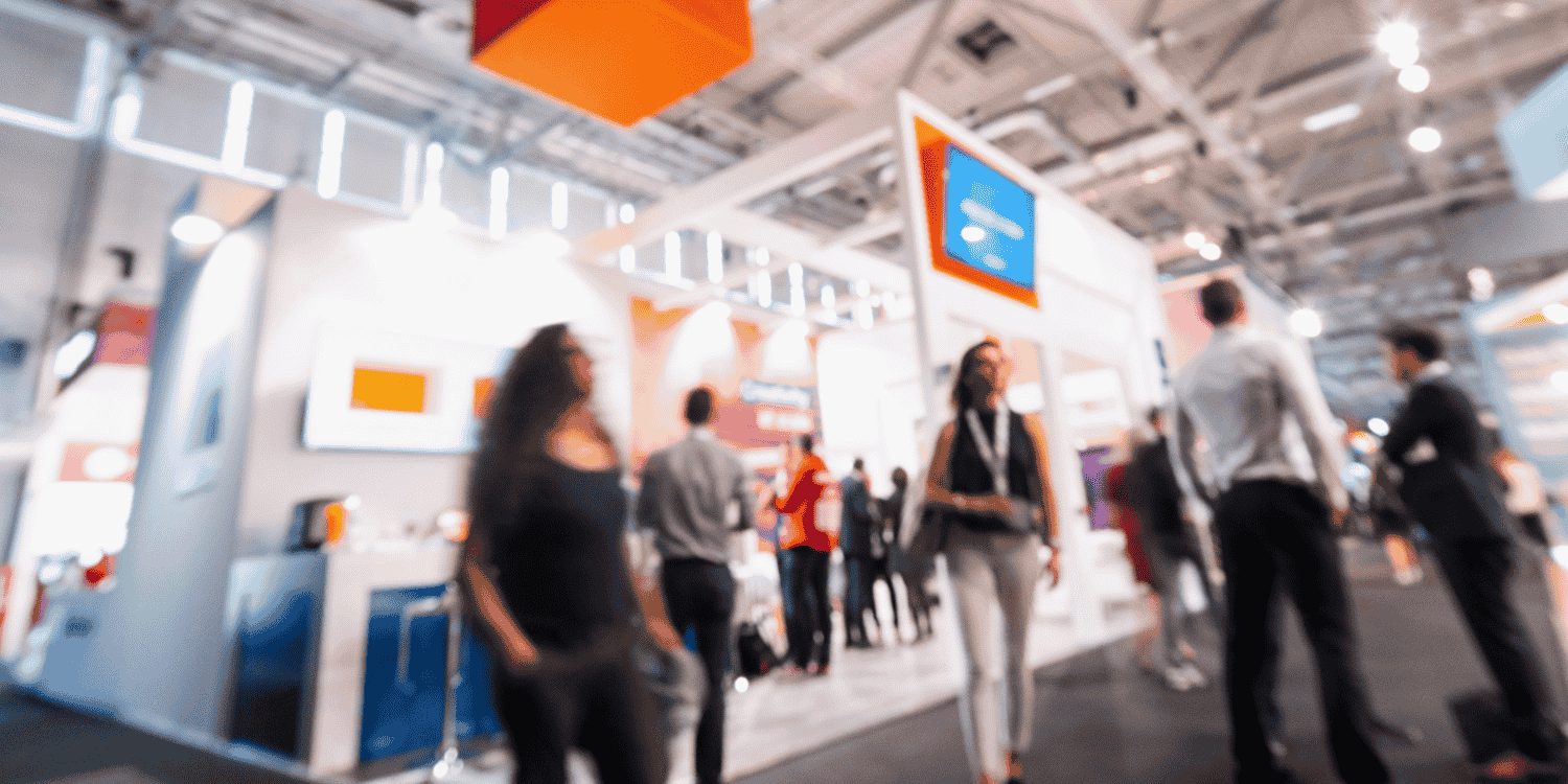 Busy trade show floor with attendees visiting branded booths, representing the need to plan and order the right quantity of corporate giveaways for maximum event impact.