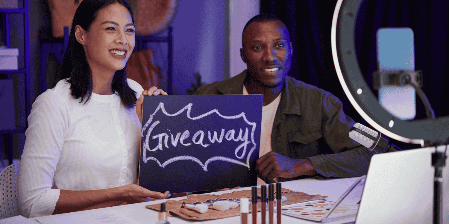 Content creators showing how to do online giveaways during a livestream, with a giveaway sign, smartphone setup, and promotional products on the table.