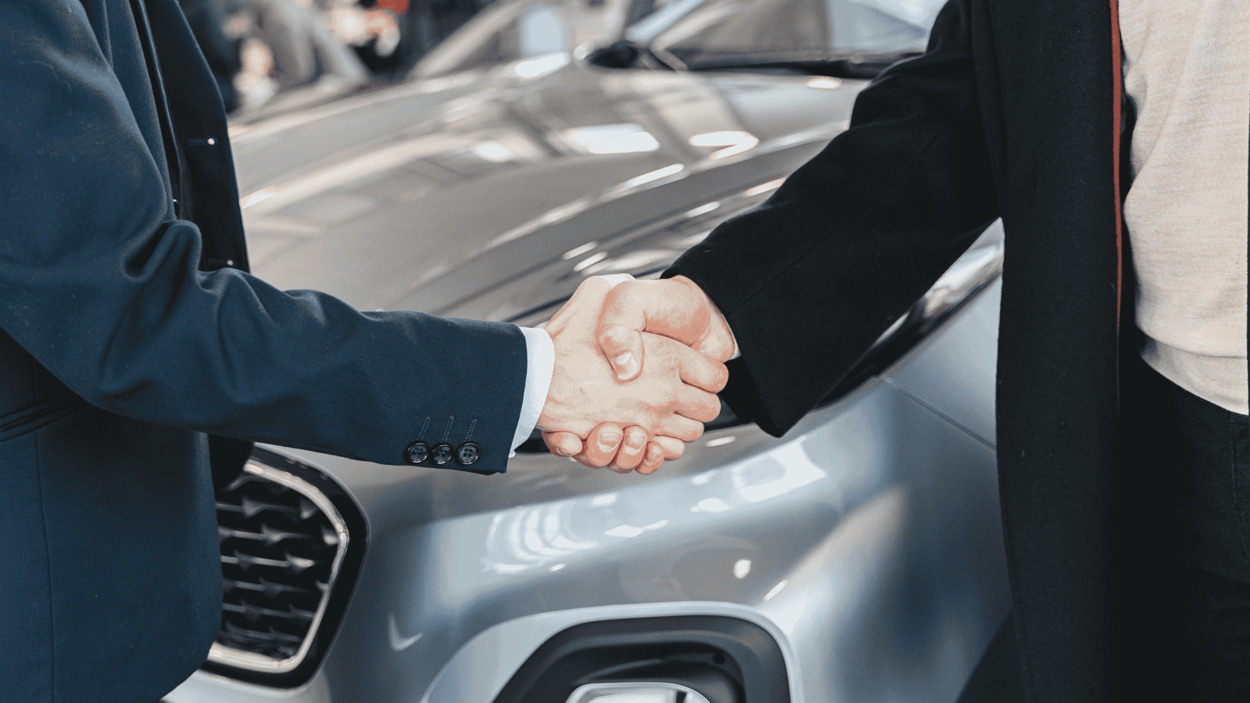 Two people shaking hands in front of a silver car, symbolising a successful agreement.